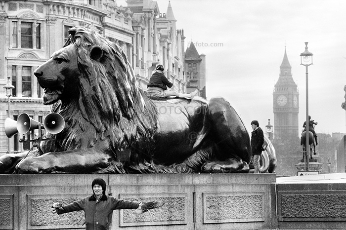 Trafalgar Square, pigeons and tourists, London. Photo image shows man with pigeons on perched on his arms in front of one of the lion statues. Photo circa 1979