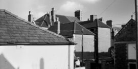 Roof tops, Roath, Cardiff, South Wales, UK. View from 126 Arabella Street, Roath showing wall, roof and signage of J Sherlock & Sons motor repair garage in foreground. In the background can be seen the rear of entrance and roof top chimneys of The Albany public house, Donald Street, Roath, CF24 4TL Cardiff, UK. Photo circa 1974-5.