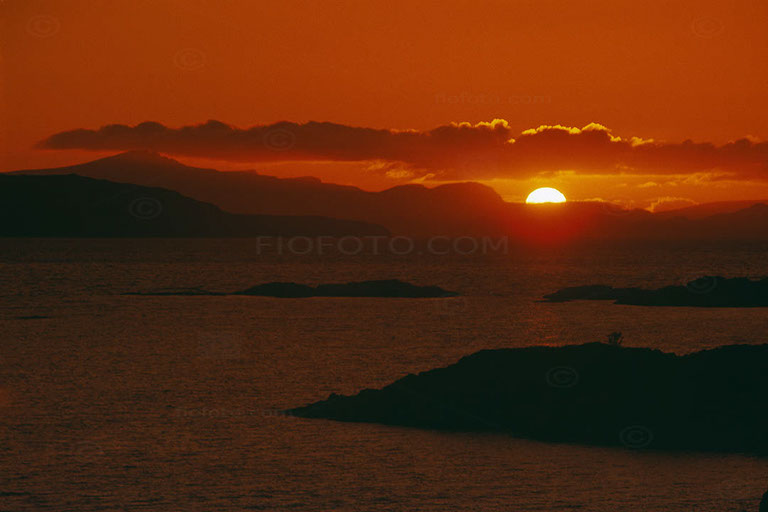 Sunset view Isle of Skye Scotland. Sun setting over Isle of Skye from west coast mainland, Scotland UK. Shows orange/red sky, small islands silhouetted.