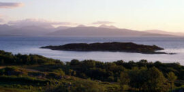 Sunset view from near the village of Kyle of Lochalch towards Isle of Skye, North Western, Scotland, UK Image shows grazing farmland in the foreground against the backdrop of sea and distant island.