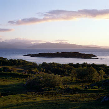Sunset view from near the village of Kyle of Lochalch towards Isle of Skye, North Western, Scotland, UK Image shows grazing farmland in the foreground against the backdrop of sea and distant island.
