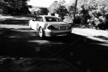 A light coloured Mercedes-Benz car, travelling at speed along a quiet, tree-lined, suburban street in Bowral, New South Wales.